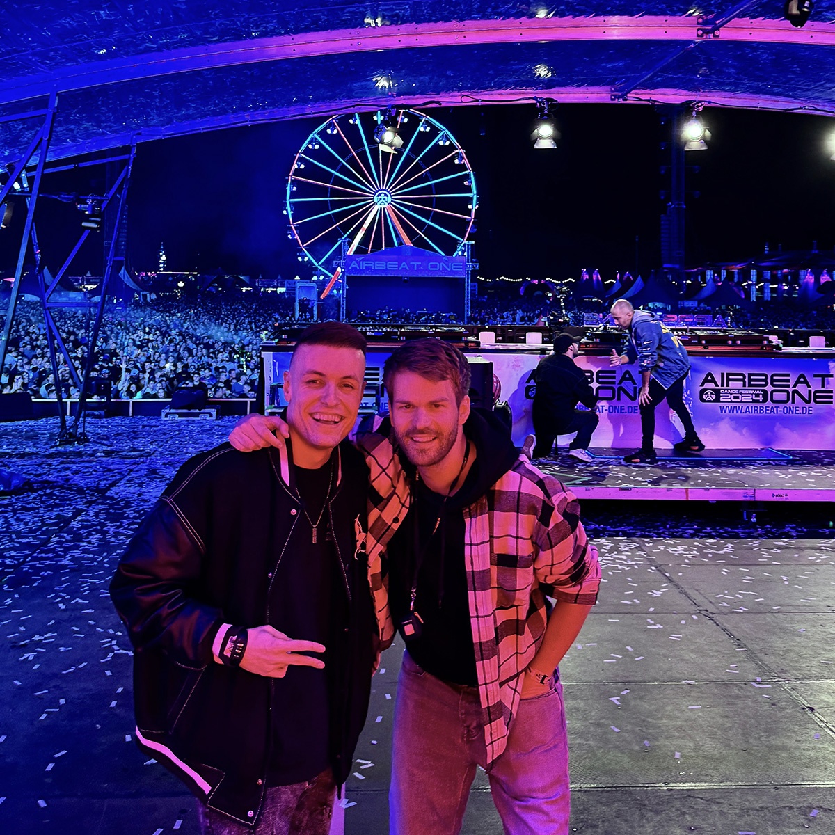 Michael Avenue and DJ colleague Tiscore standing on the Airbeat One stage behind the DJ booth, with a crowd of 30,000 people in the background.