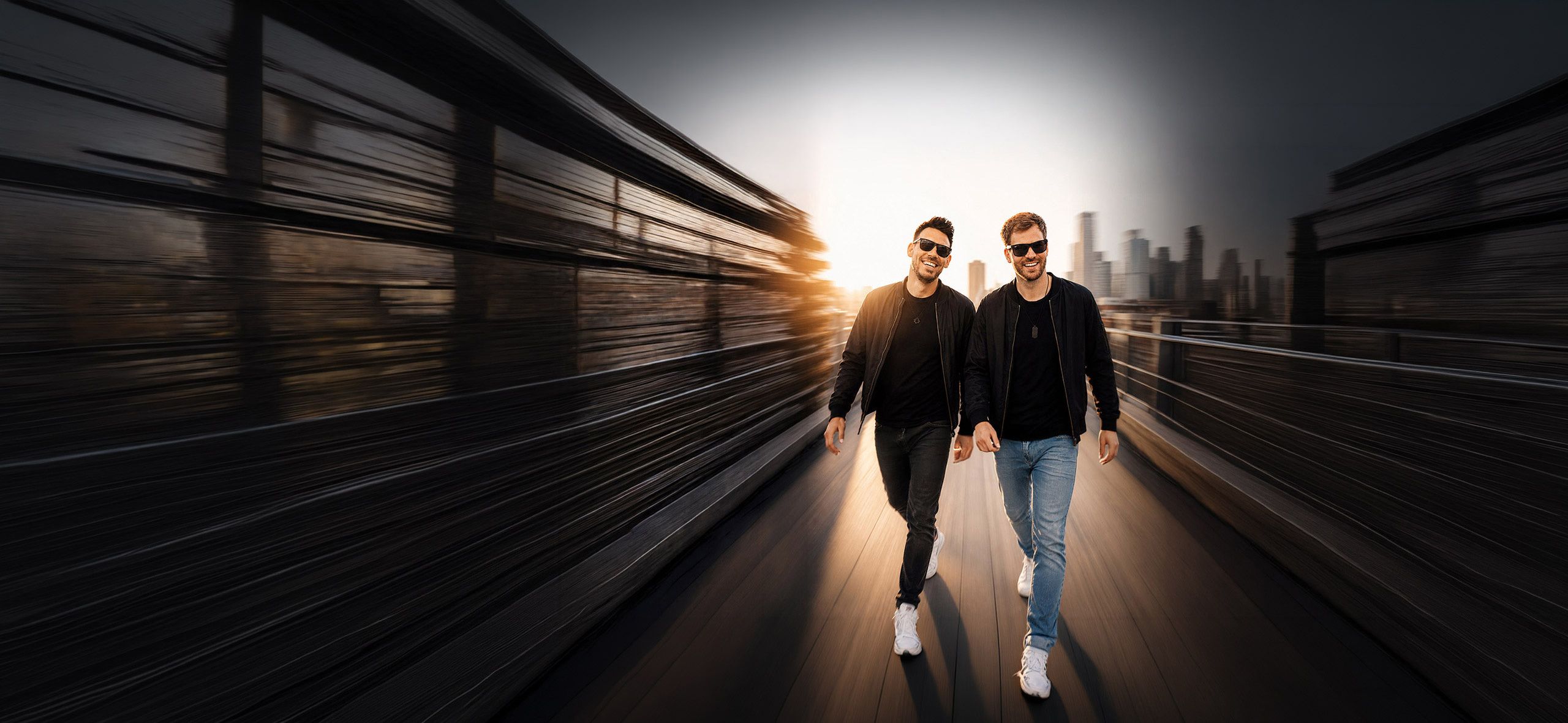 Topmodelz – Michael Avenue and Marvin Mash walking across a bridge at sunset with the city skyline behind them